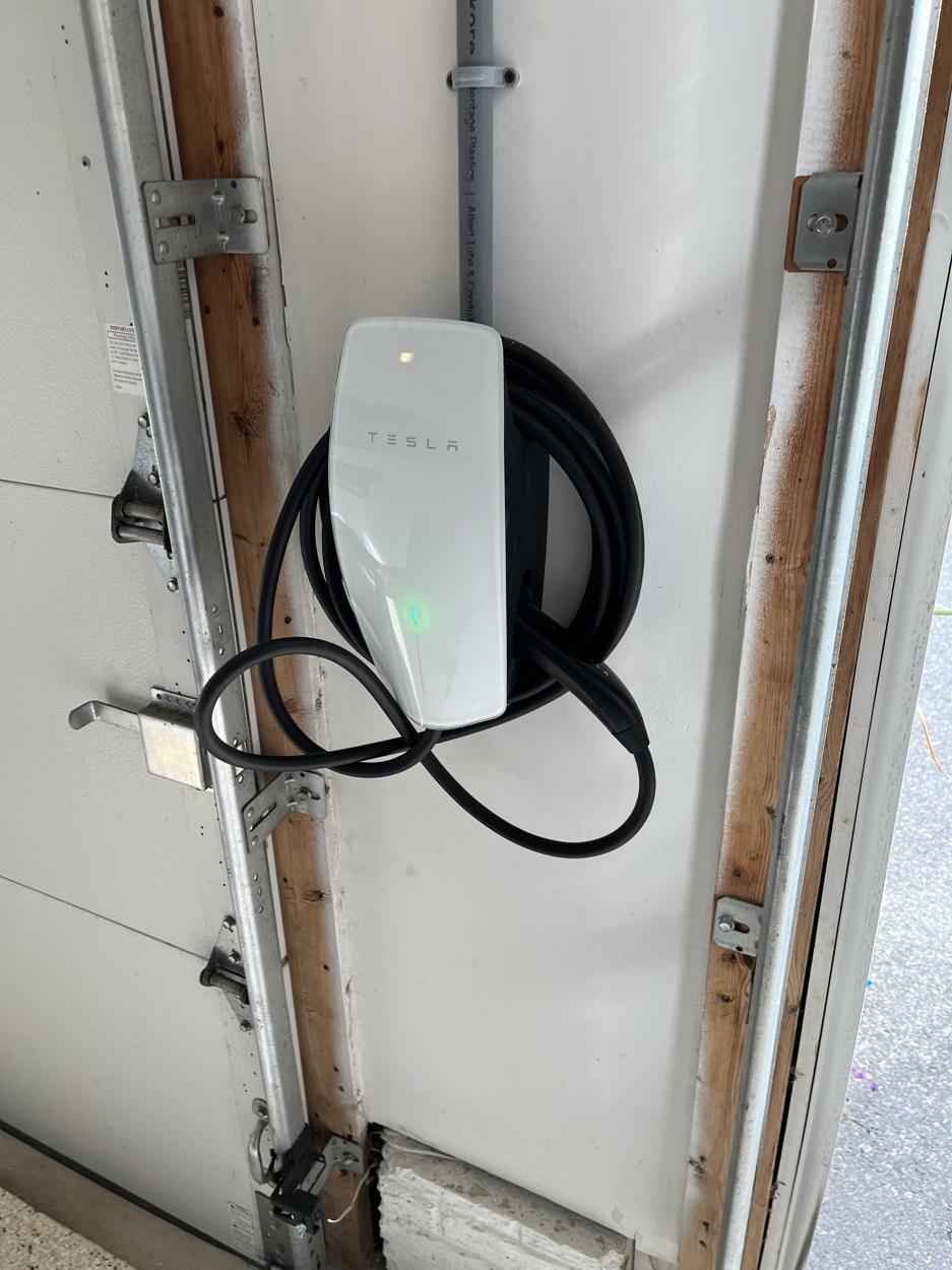 A Tesla Wall Connector EV charger mounted on a garage wall