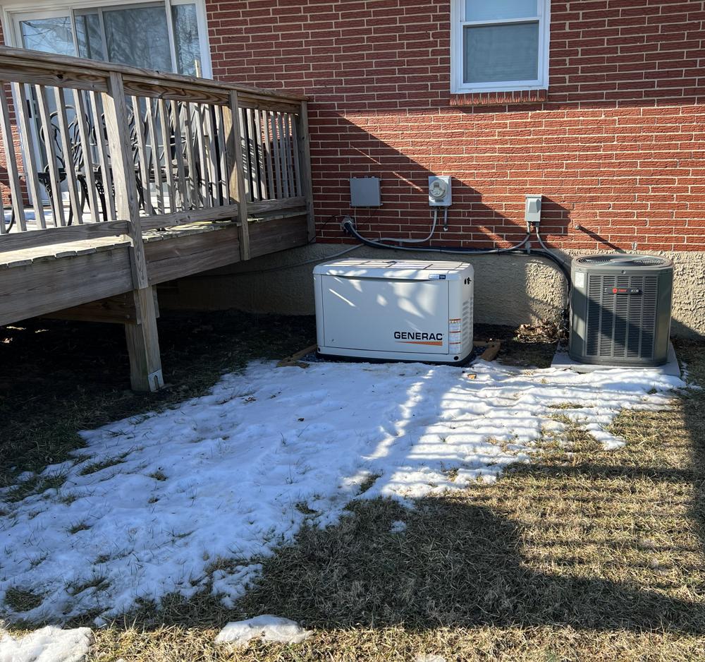 A Generac standby generator installed beside a brick house next to the air conditioner